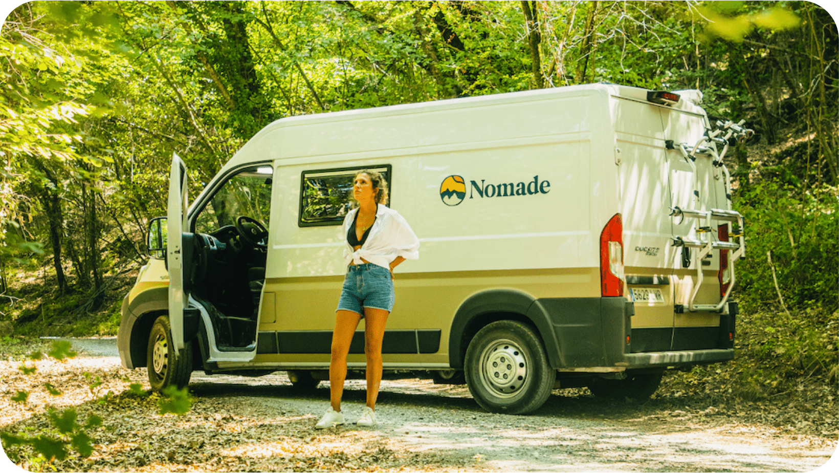 Chica con una furgoneta camper en una carretera en medio del bosque 